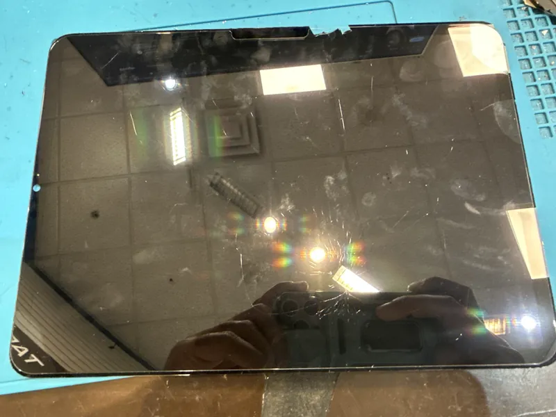 A tablet with cracked and scratched glass on a blue repair mat